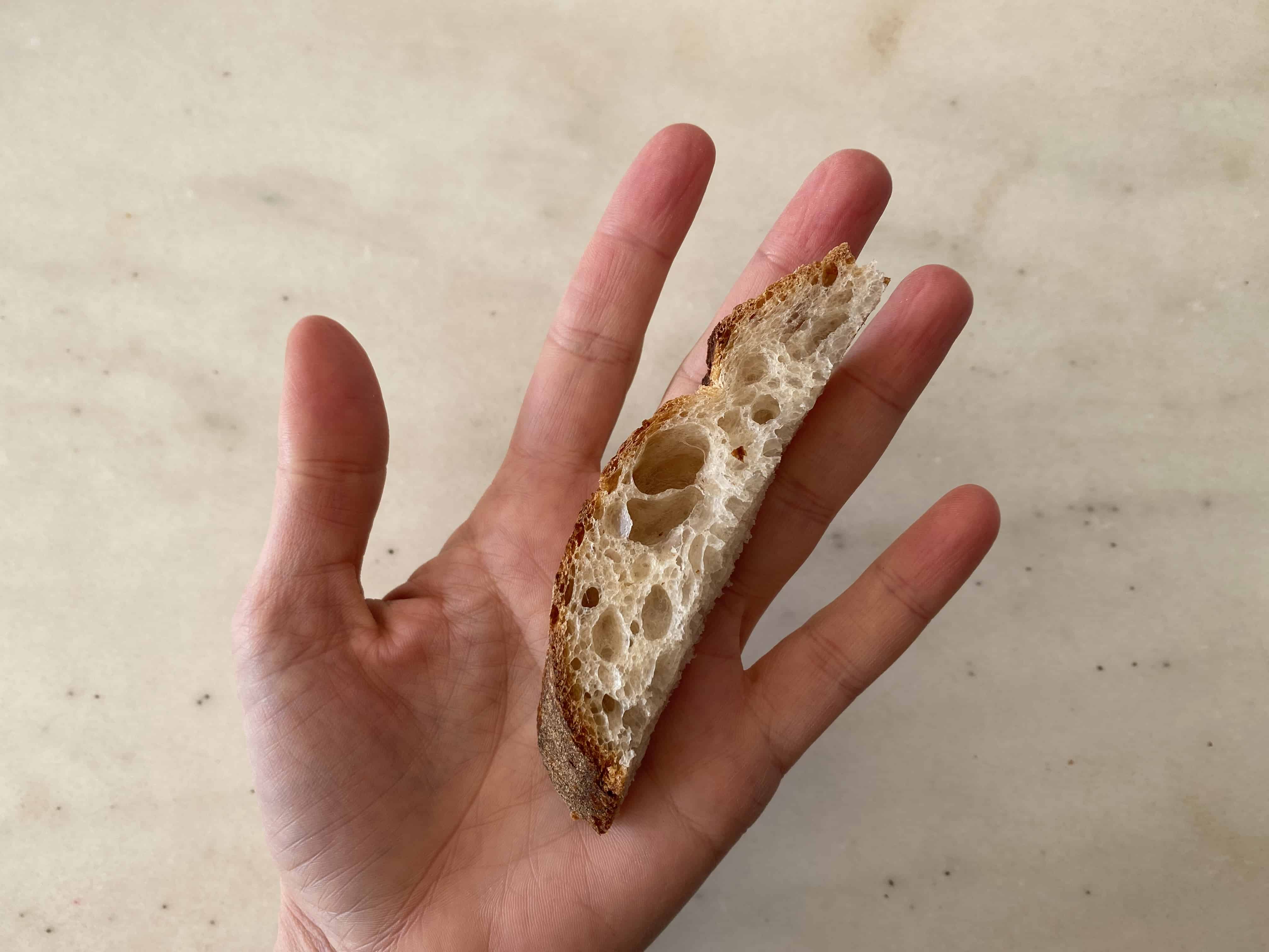 a hand holding a crusty end of bread for babies 6 months+