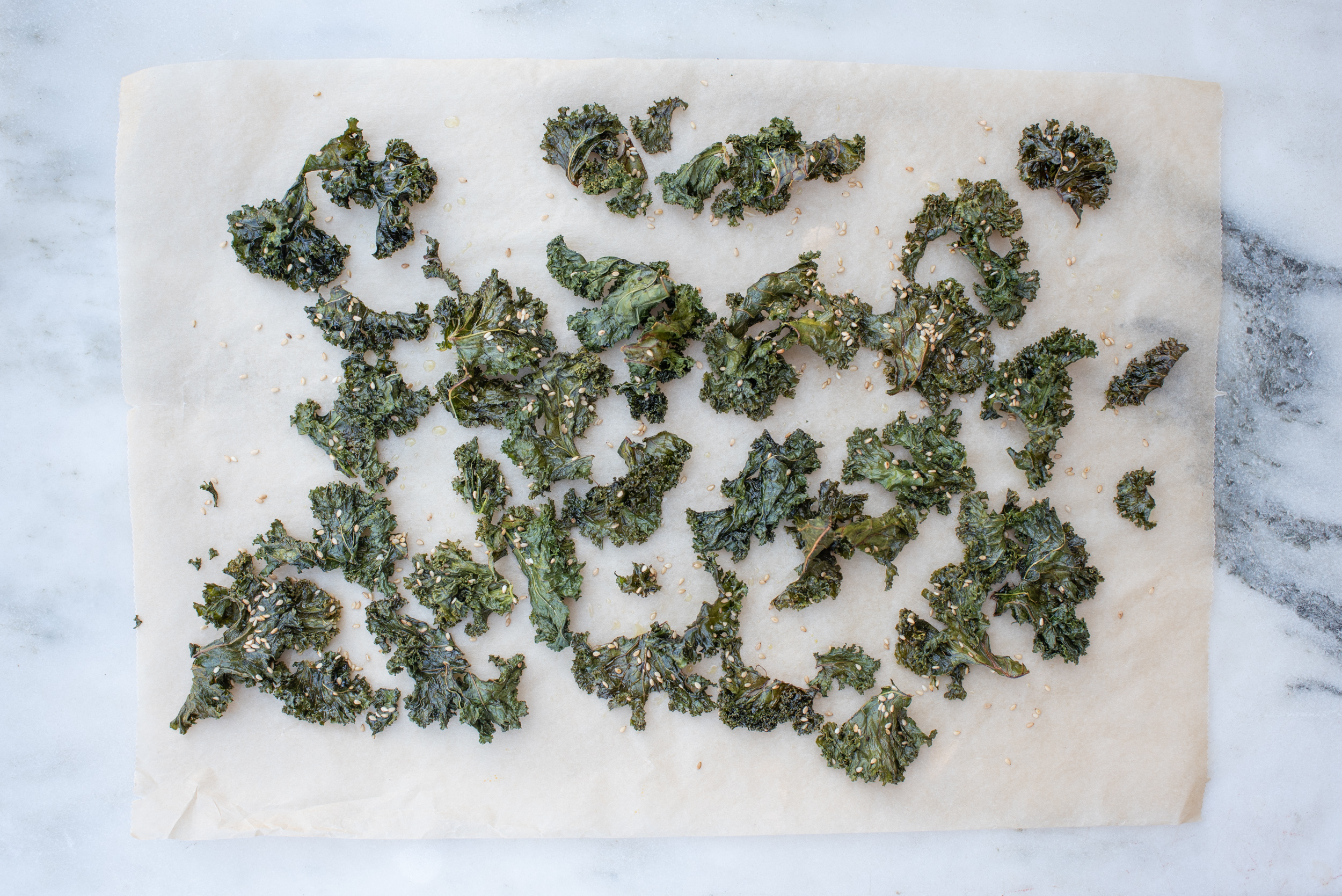 kale chips on a piece of parchment paper laid on a white marble surface