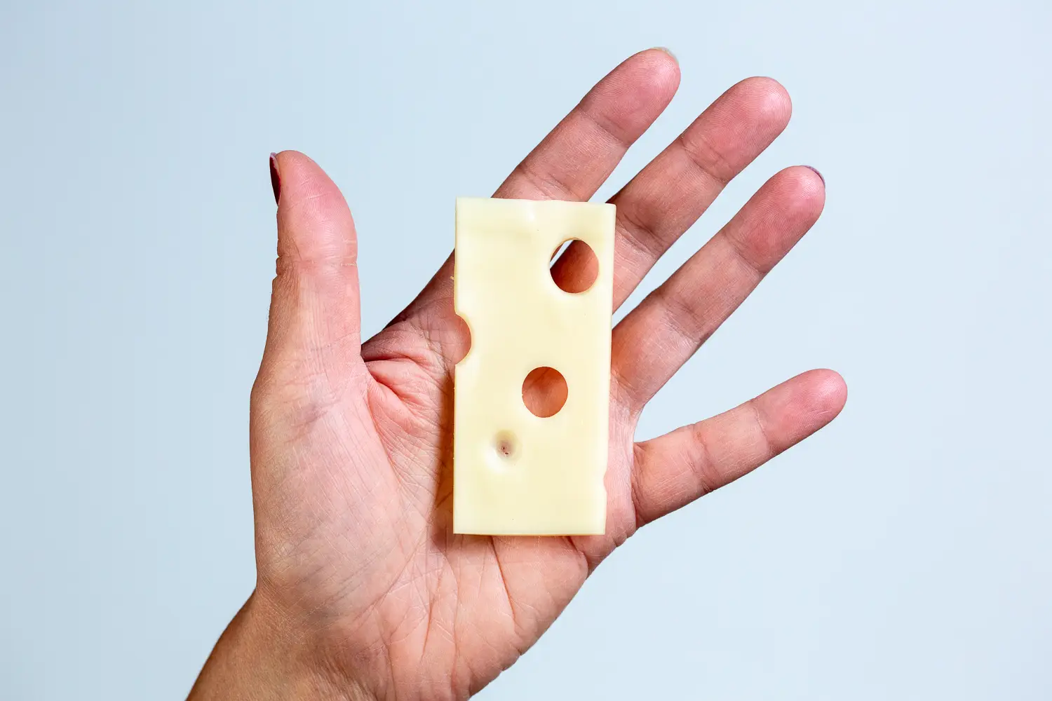 a hand holding a thin slice of emmentaler cheese for babies 6 mos+