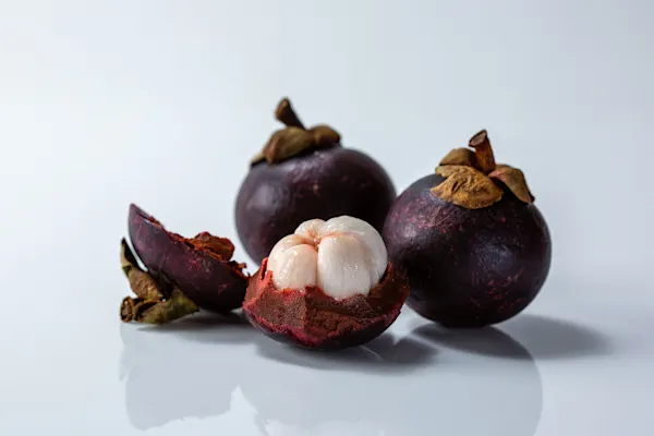 a photograph of a few whole mangosteen, one with the skin removed from the top part to show the white fruit inside