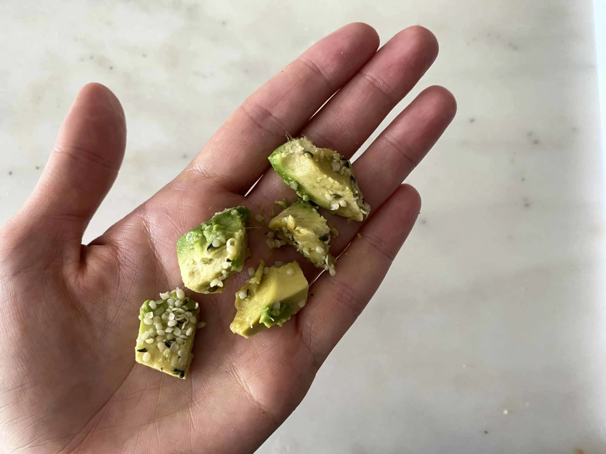 hand holding pieces of avocado with hemp seed on them