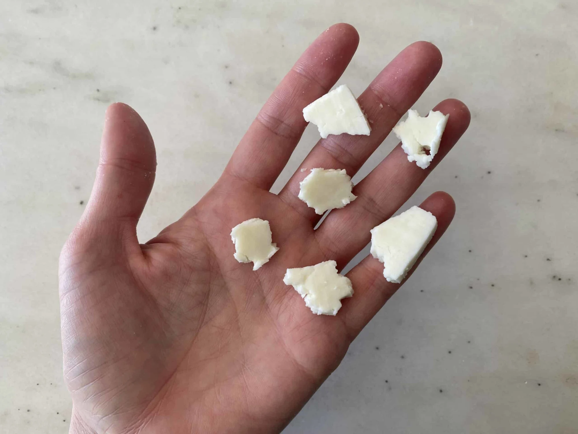 a hand holding six bite-sized pieces of paneer cut from a thin slice for babies 9 months+