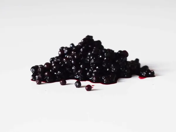 a small pile of elderberries with a bit of pink juice at the base on a white background