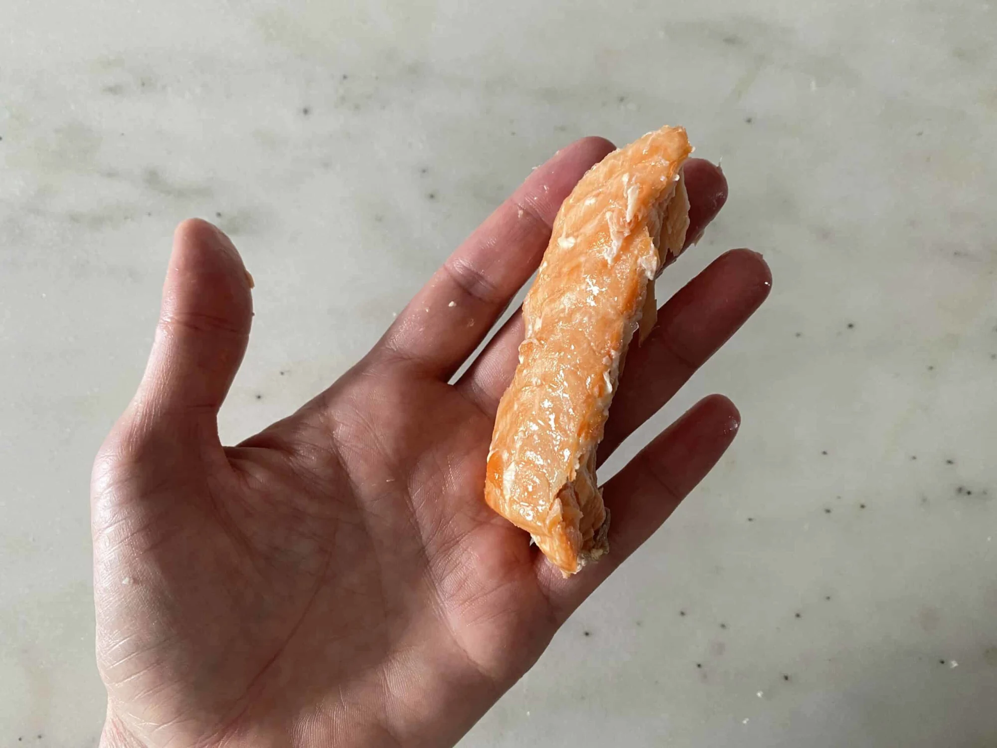 a hand holding a boneless sardine fillet about the size of two adult fingers held together for babies 6 months +