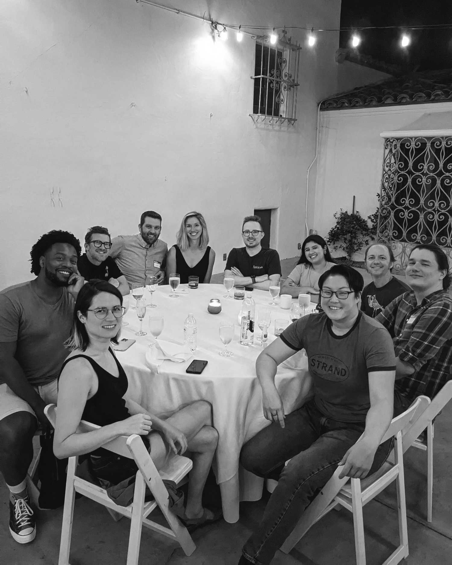 A group of people sit around a dinner table, smiling at the camera.