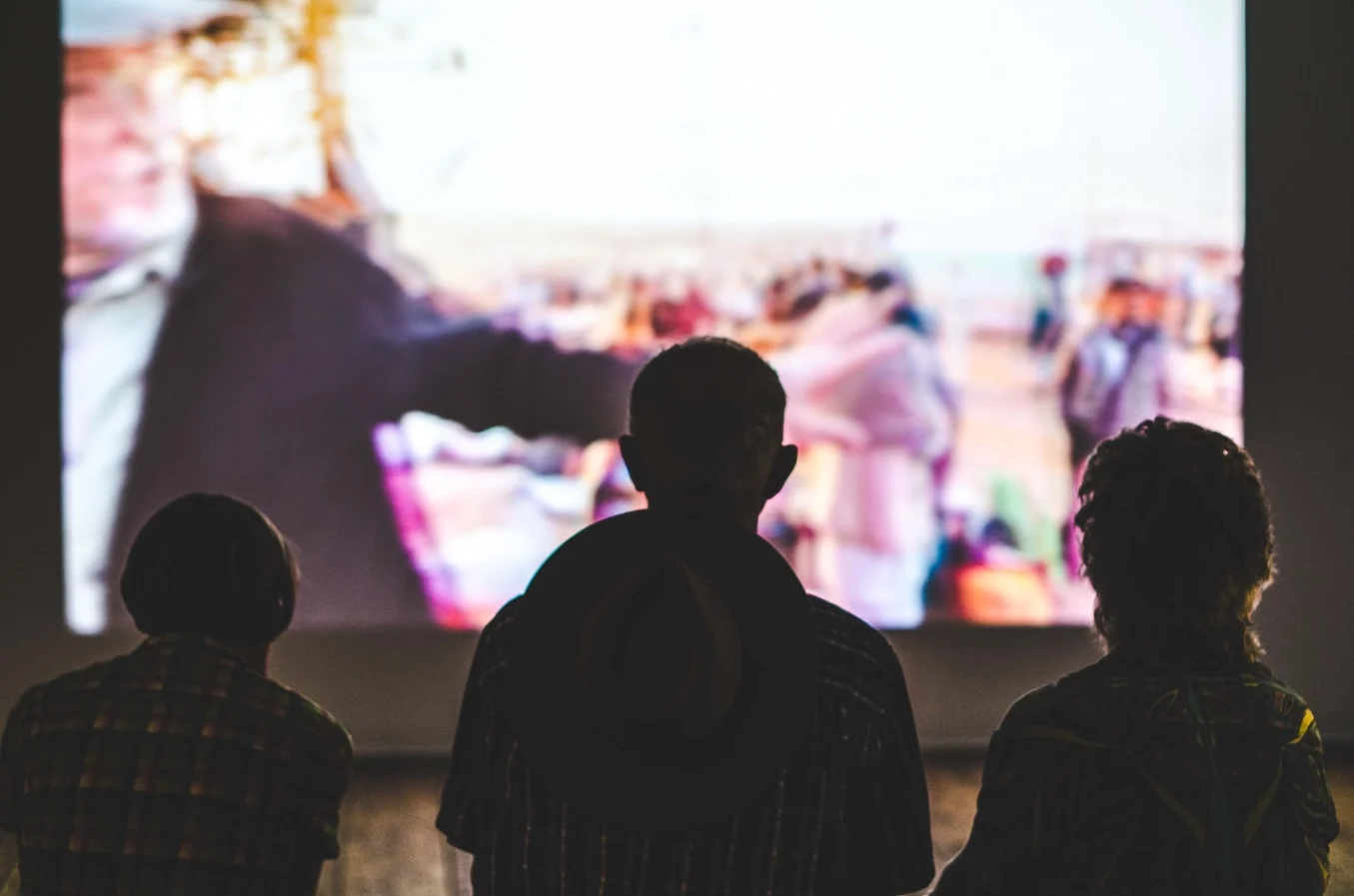 Three people are watching a movie on a big screen with their backs turned away from the camera