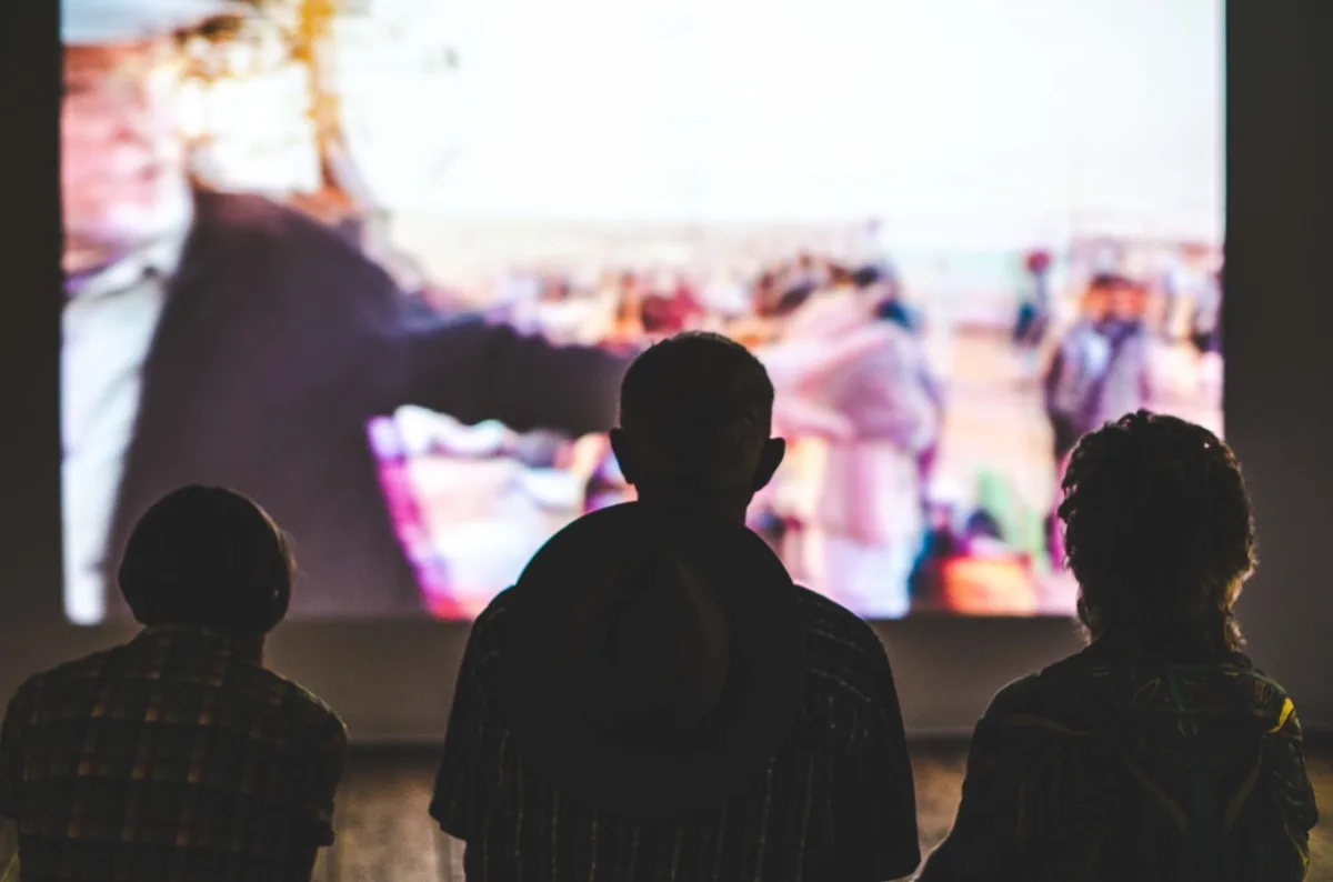 Three people are watching a movie on a big screen with their backs turned away from the camera