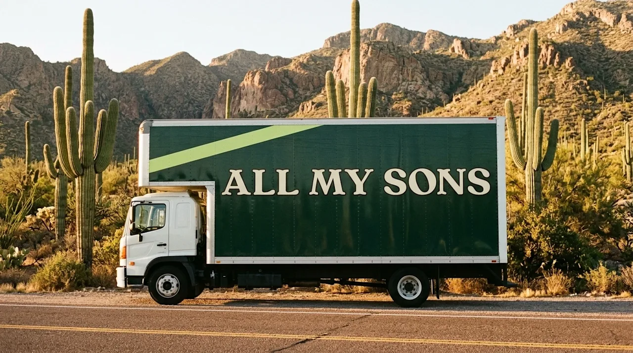 A cinematic, warm lifestyle photograph of an All My Sons moving truck parked along a scenic road surrounded by the natural wo