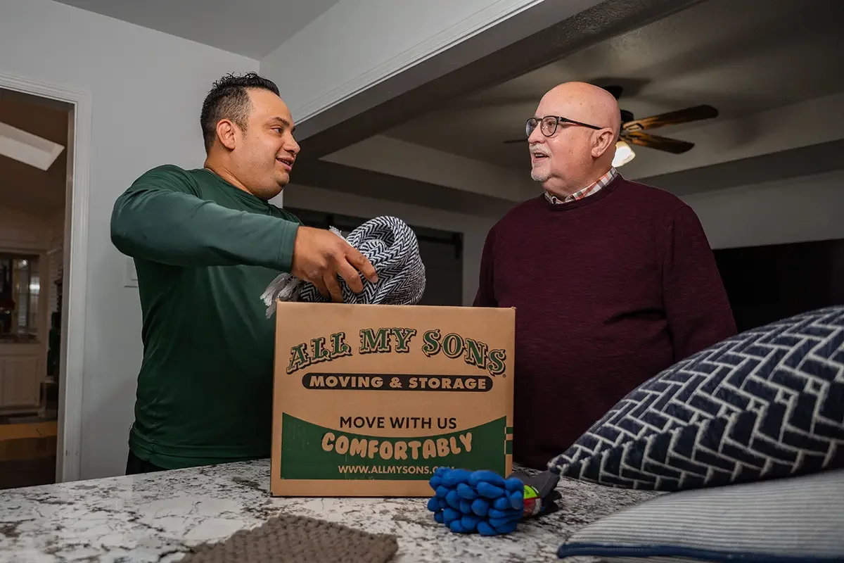 All My Sons professional packer puts blankets in a moving box while he talks with the customer.