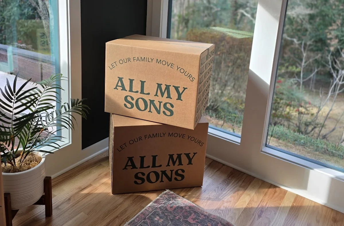 All My Sons Moving & Storage boxes stacked in the corner of a living room awaiting movers to pack them.