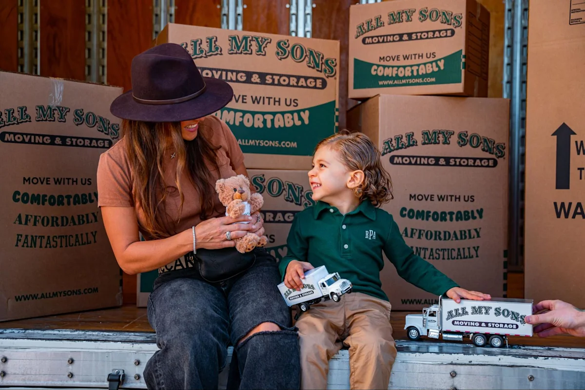 Mother and son play with toy All My Sons moving trucks in the back of a real moving truck.