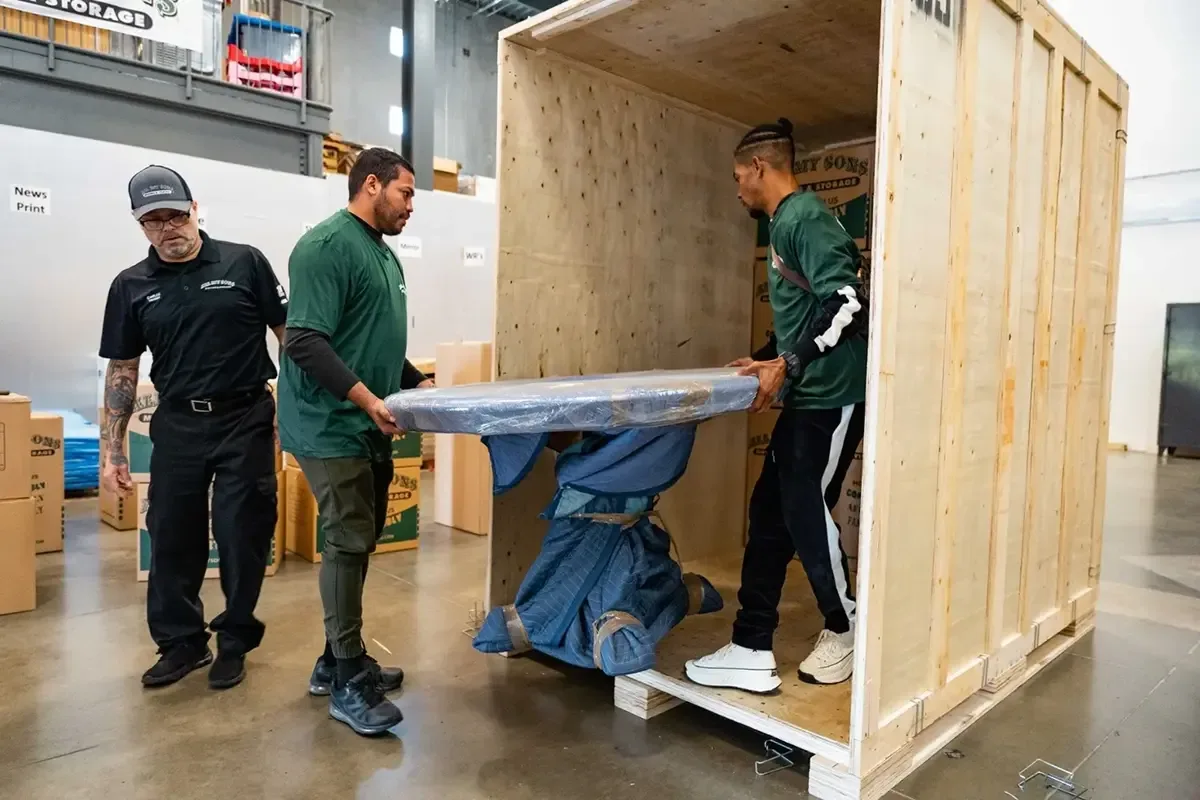 All My Sons team members move a wrapped table into storage.