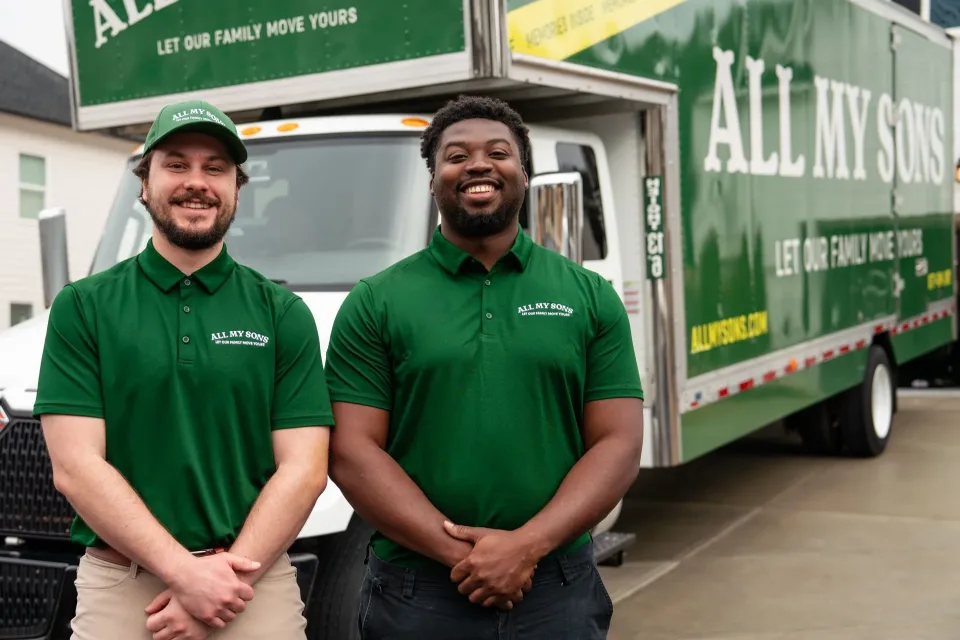 Two happy All My Sons Moving and Storage employees stand beside an All My Sons Moving Truck.