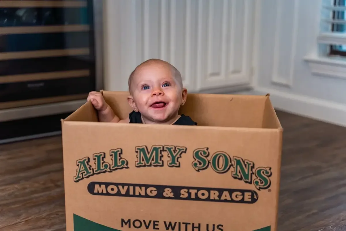 Toddler peeks out of an unpacked All My Sons moving box.