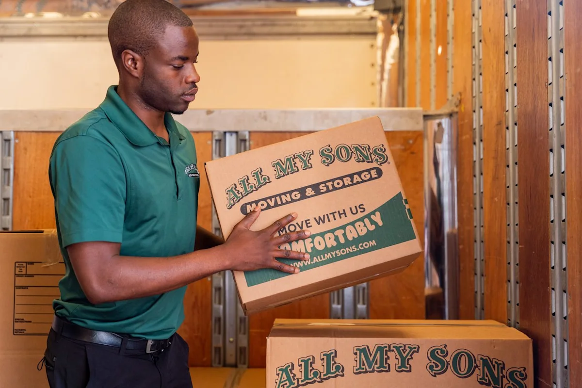 An All My Sons mover lifts a moving box packed with shoes.