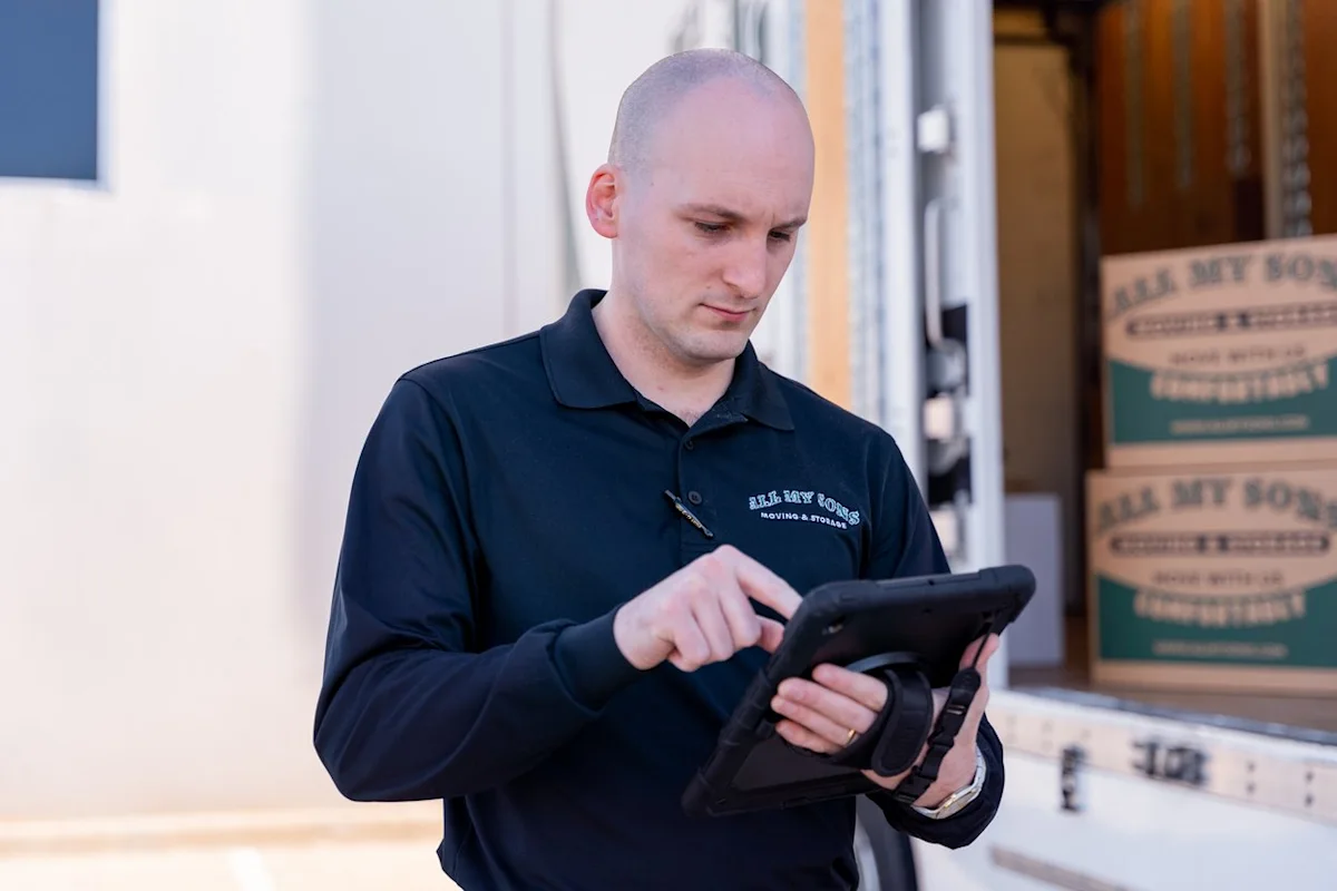 A professional mover from All My Sons Moving and Storage checks his tablet before closing a moving truck.