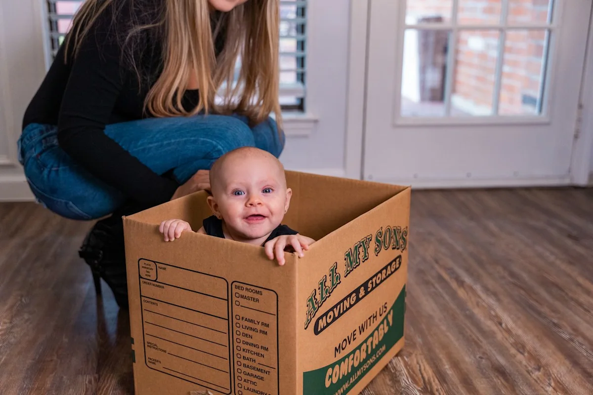 A mother watches over a toddler as she plays in an All My Sons Moving and Storage moving box.