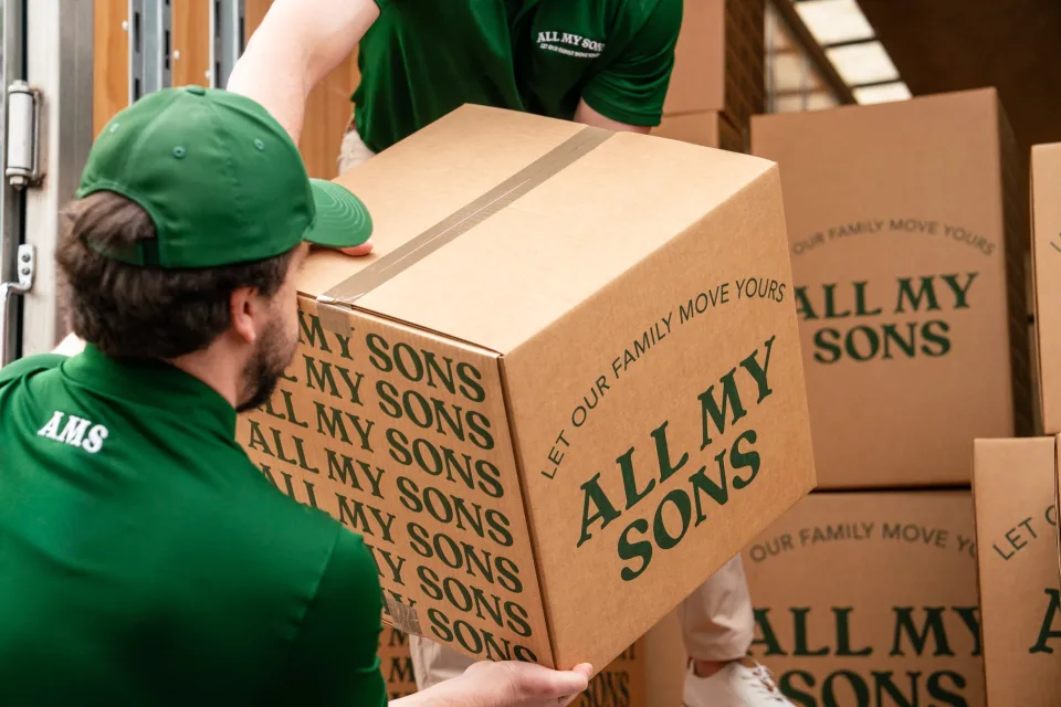 Two movers lift a box into an All My Sons Moving truck.