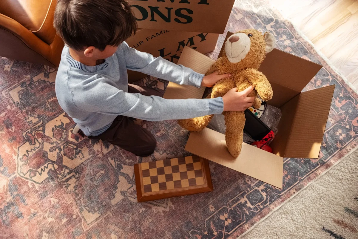 Young boy puts away stuffed toy in an All My Sons Moving and Storage box.