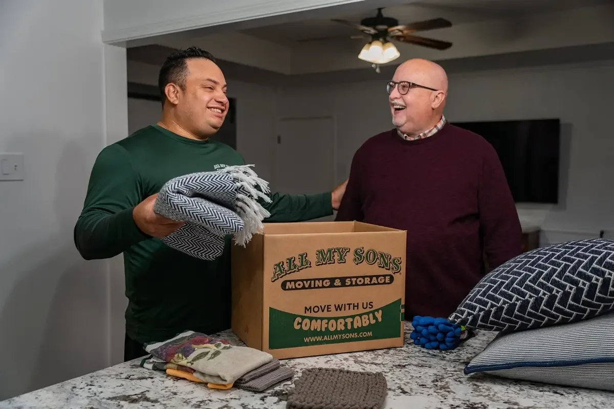 All My Sons professional packer puts a friendly hand on a customer's shoulder while loading a moving box.