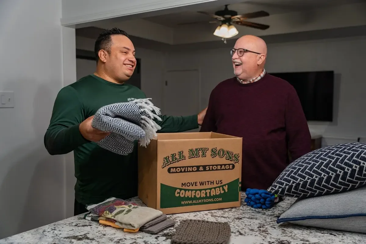 All My Sons professional packer puts a friendly hand on a customer's shoulder while loading a moving box.