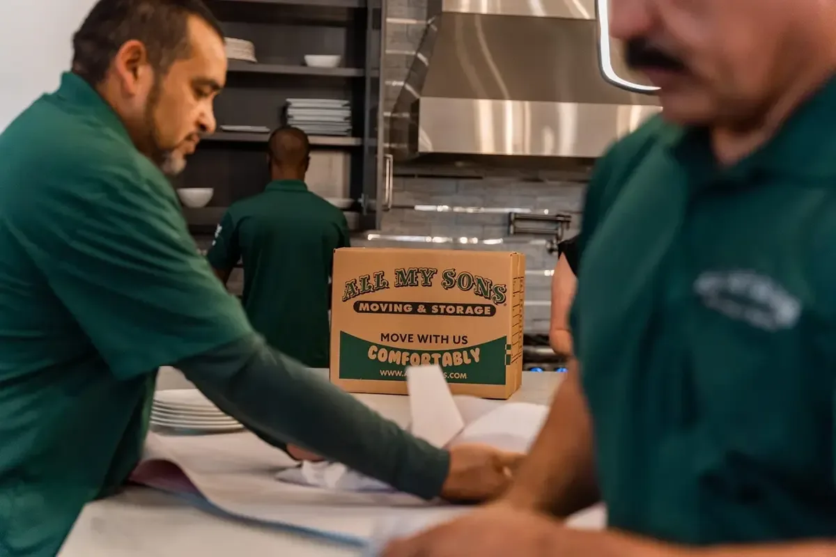 Professional packers with All My Sons wrap plates and dishes for loading into moving boxes.