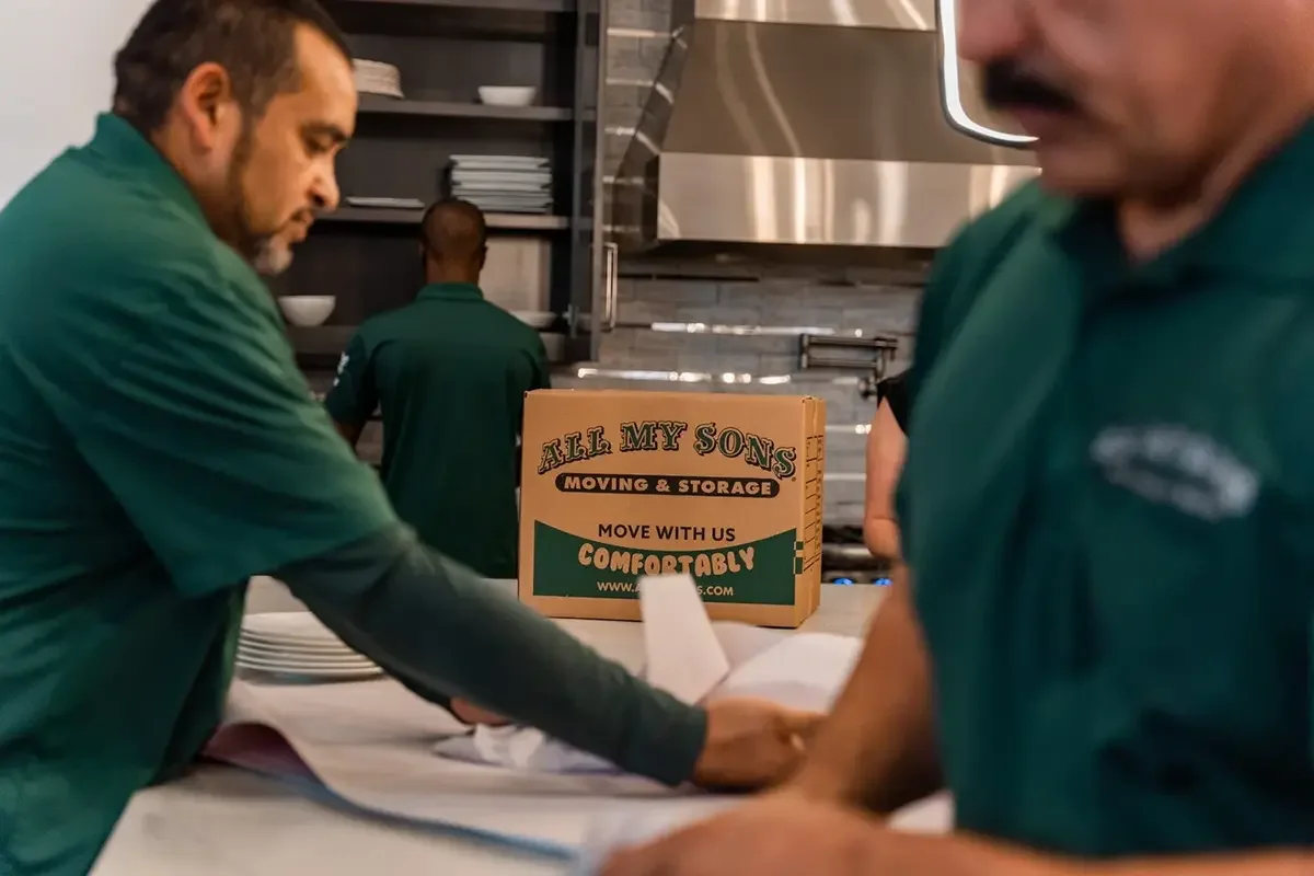 Professional packers with All My Sons wrap plates and dishes for loading into moving boxes.