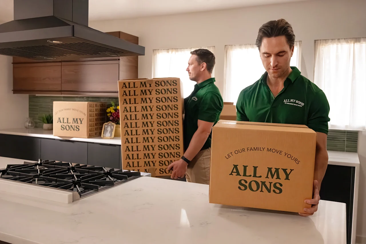 A pair of All My Sons movers take a few moving boxes from a kitchen. 
