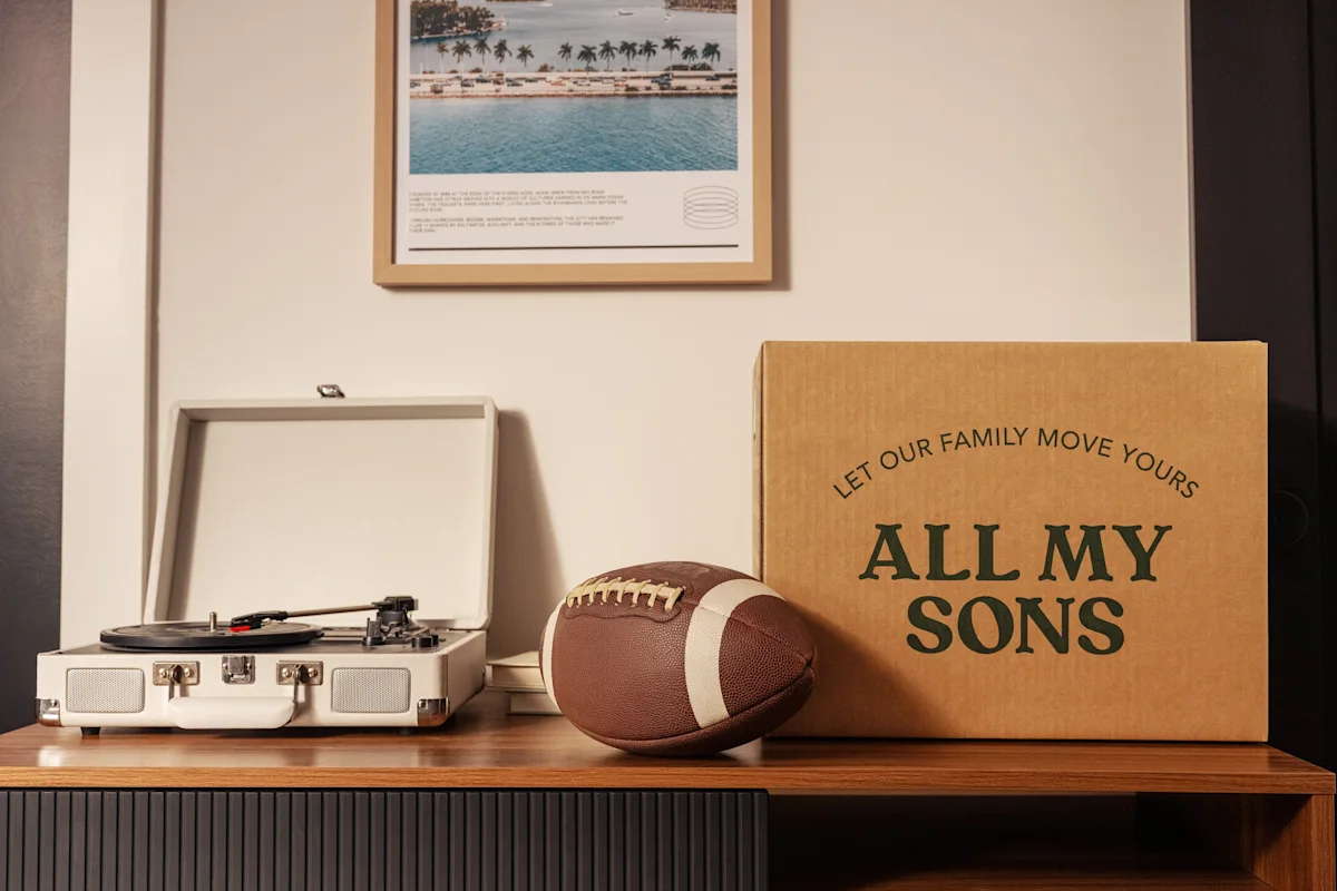 An All My Sons moving box next to a record player and a football on the dresser of a boy moving out for college.