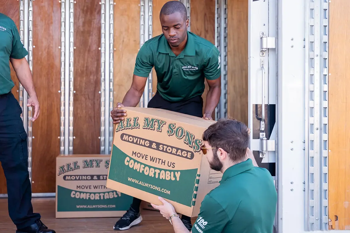 Professional movers move a small box into the back of a moving truck.