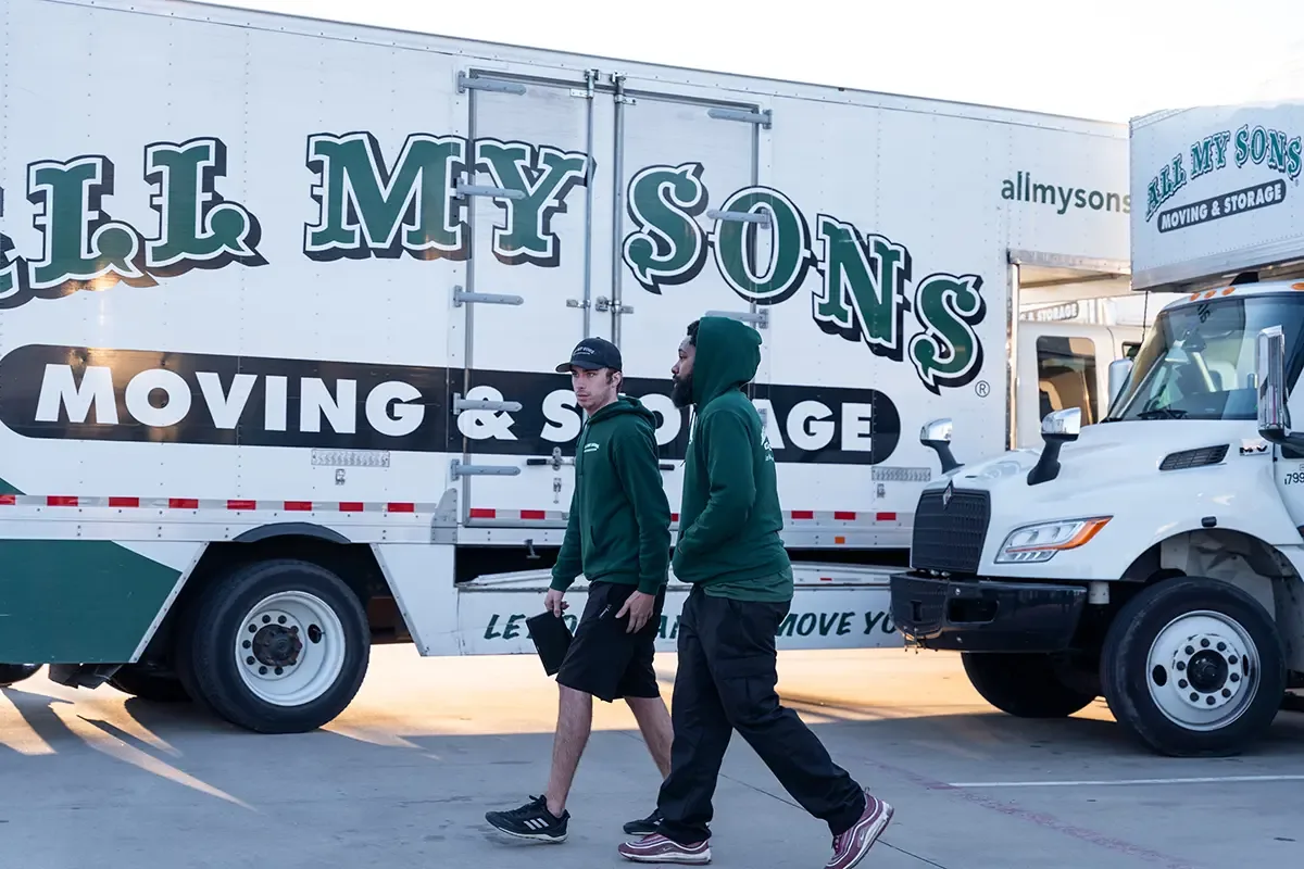 Professional movers from All My Sons Moving and Storage walk by an All My Sons moving truck to prepare for a peak season move.