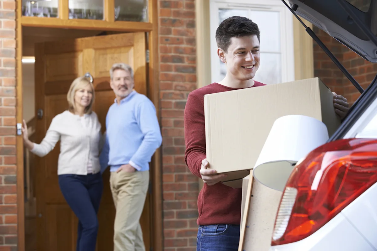 Parents watch as young adult son loads a car for a move to college.