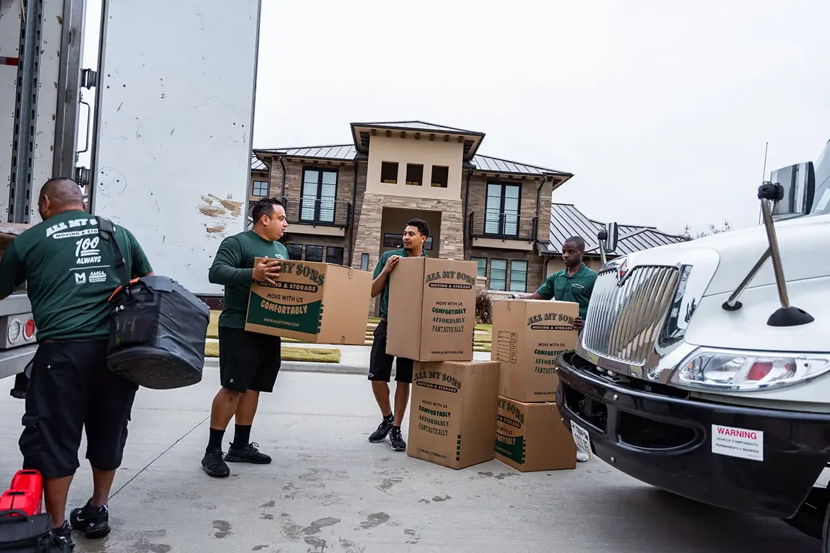 Professional movers from All My Sons carry moving boxes out to a moving truck.