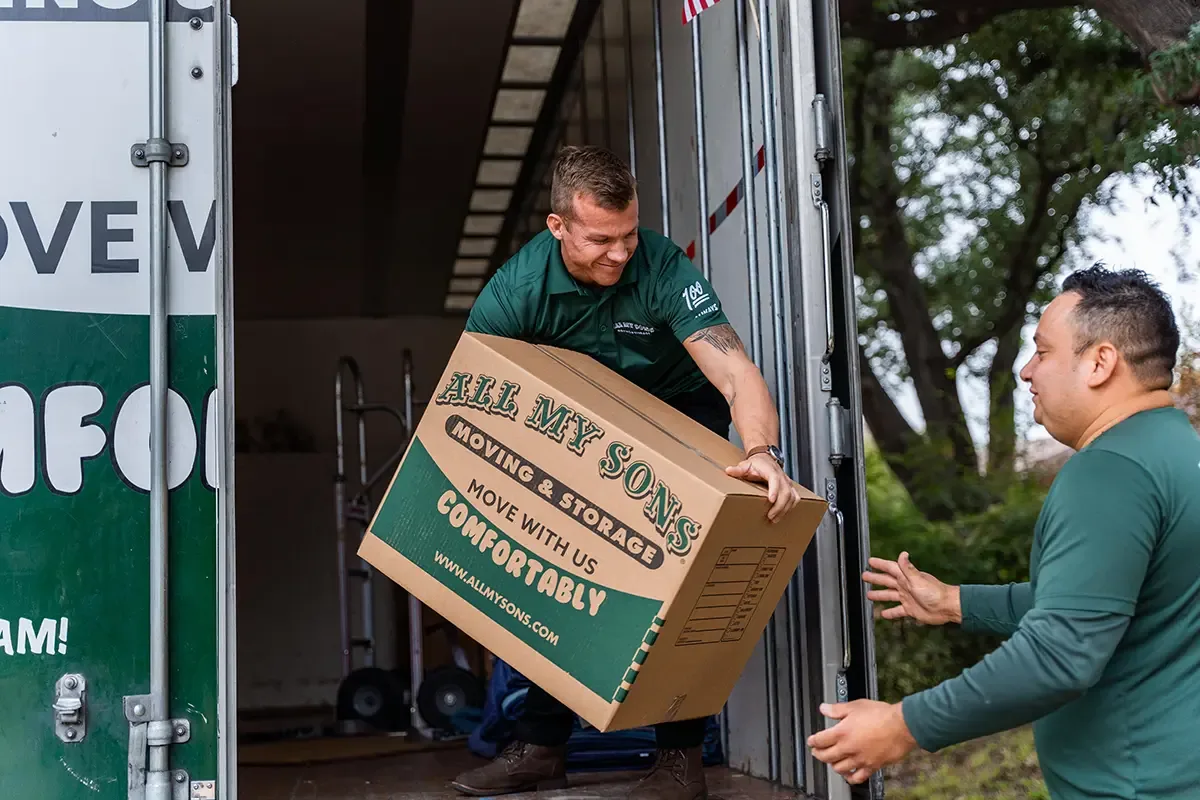 Professional movers from All My Sons load a well-packed moving box on the back of a truck.