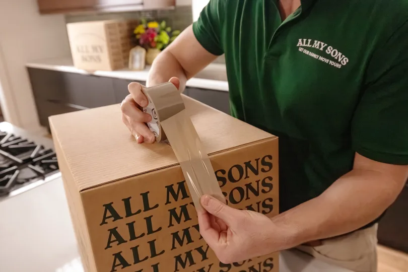 An All My Sons team member tapes a moving box shut.