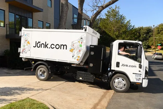 Junk.com junk truck pulling out of the driveway of a residential home after a same-day junk removal job.