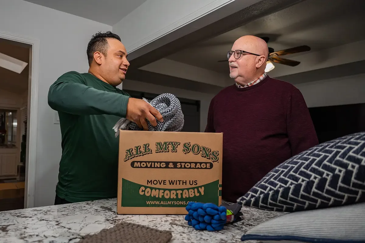 All My Sons professional packer puts blankets in a moving box while he talks with the customer.