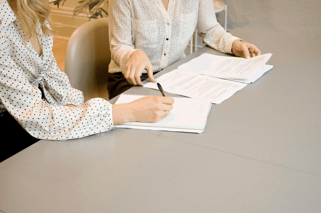 Two women sit, one signs contract