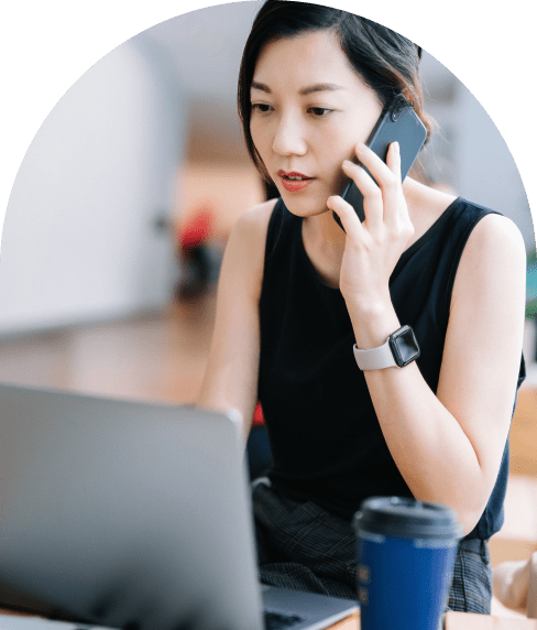 Woman on the phone and looking at her laptop working with a coffee by her side