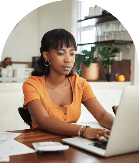 Woman at a large desk working on her laptop with papers and a calculator on the table