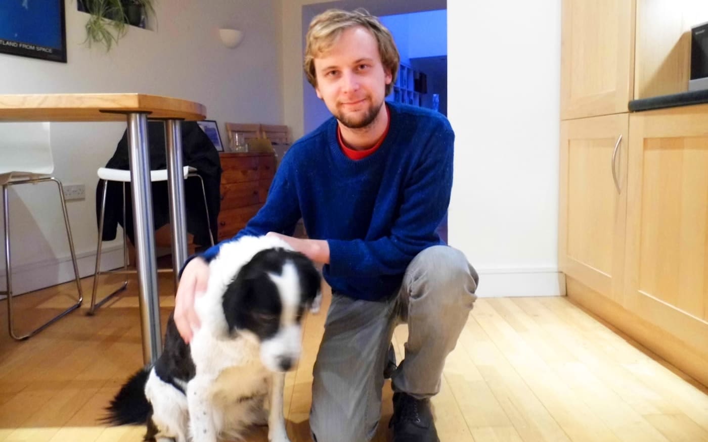 Man in blue jumper kneeling with dog 