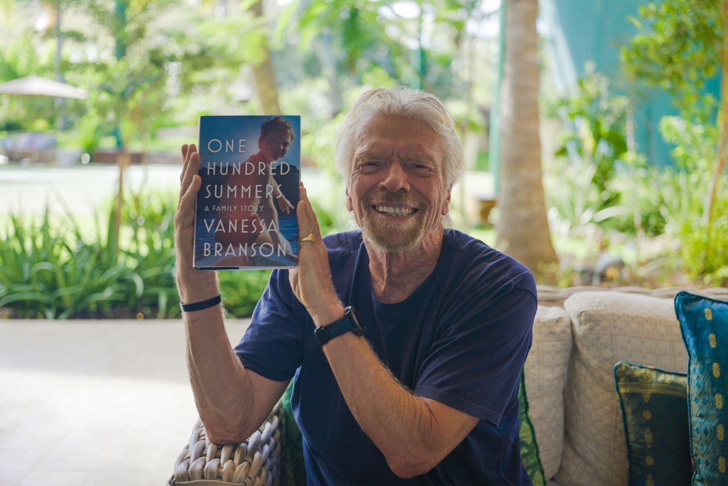 Richard Branson smiles while holding up One Hundred Summers - a book by Vanessa Branson
