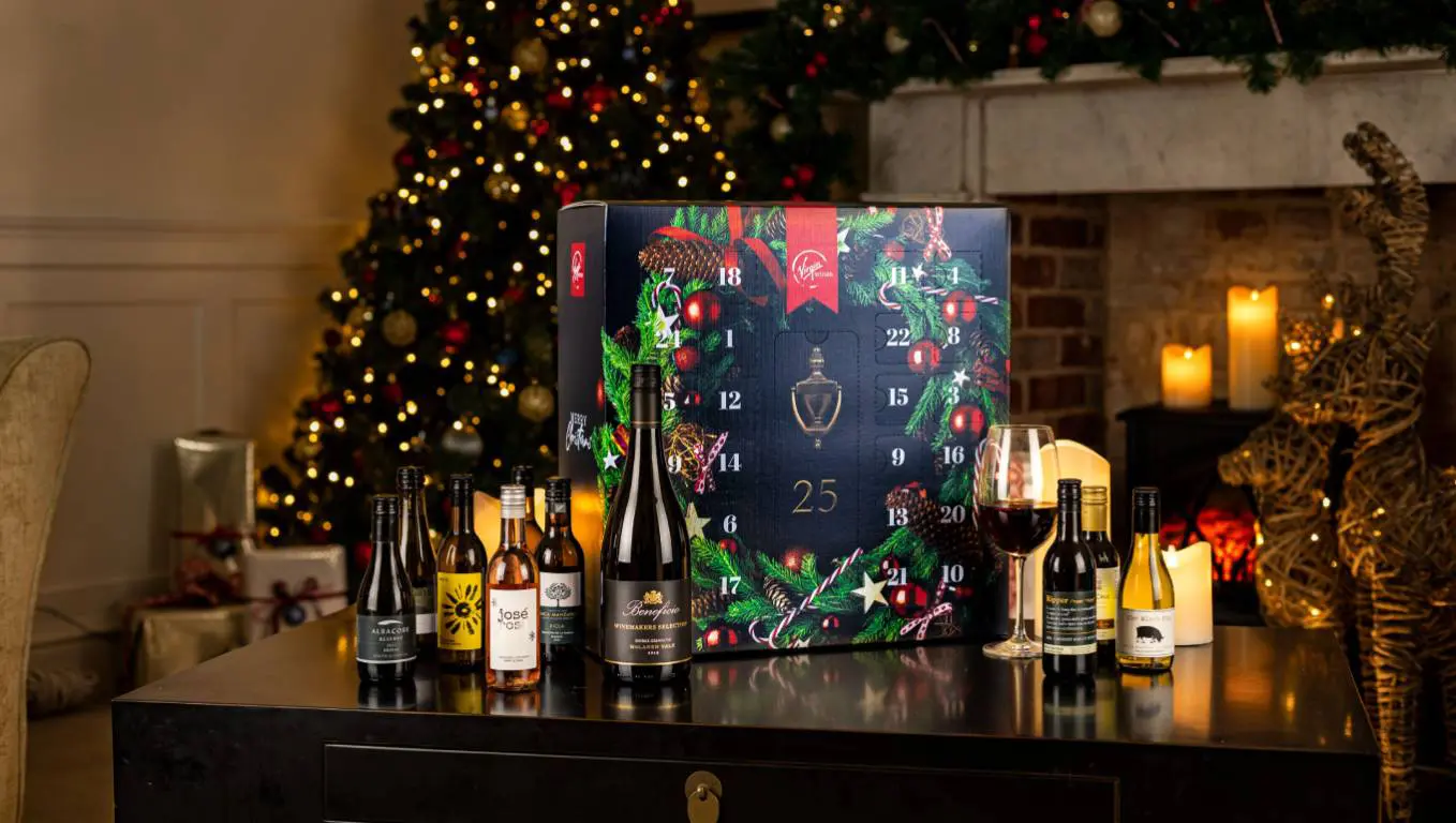 A Virgin Wines wine advent calendar next to bottles of wine on a table, in front of a Christmas tree and fireplace