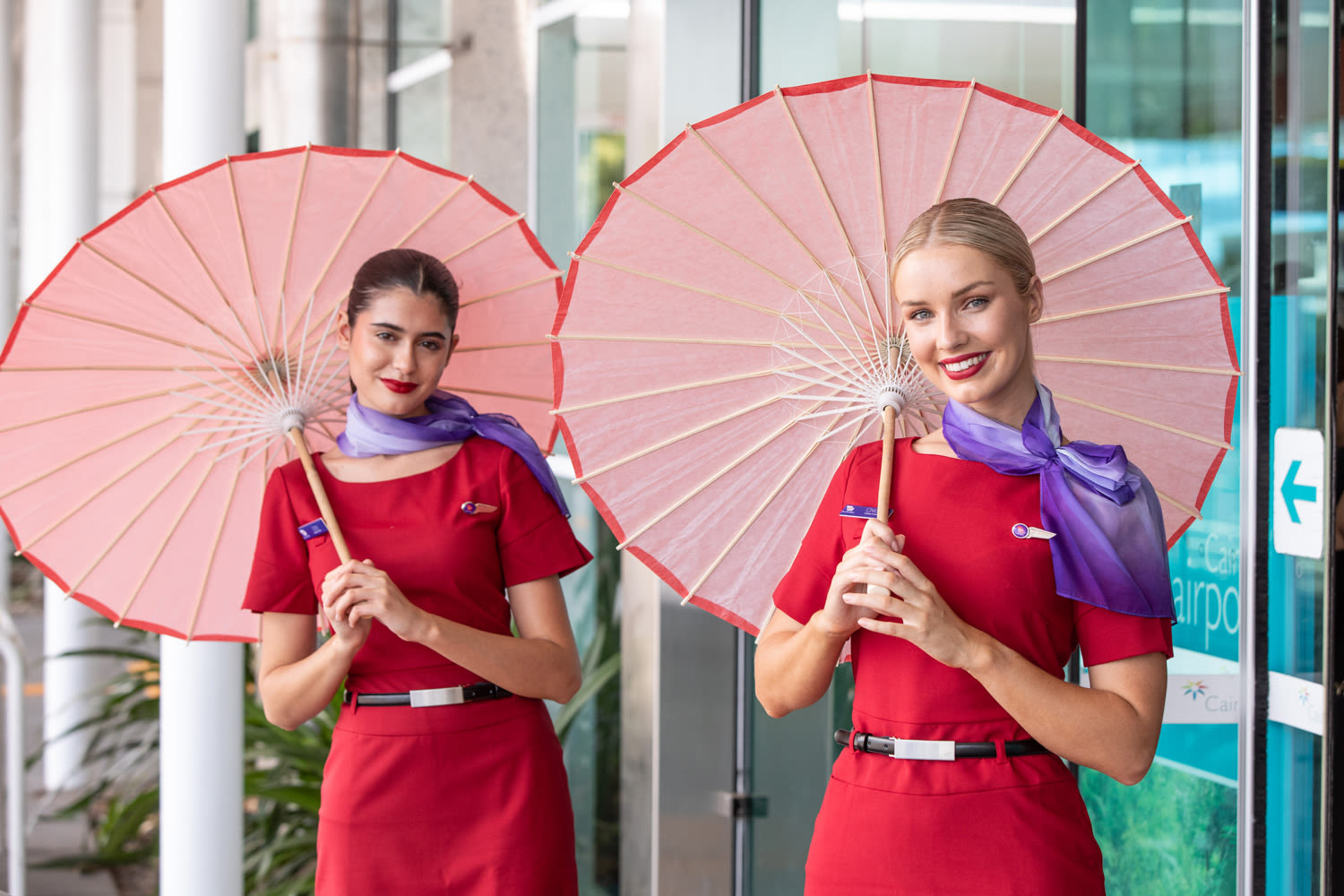 Two Virgin Australia cabin crew members holding pink and red parasols