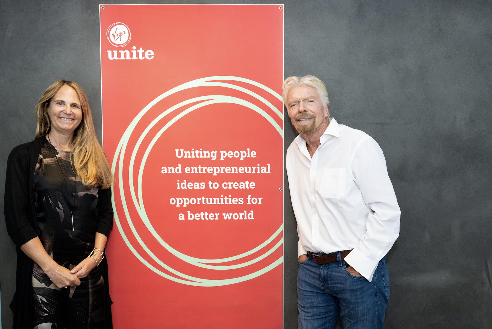 Richard Branson smiling in front of a Virgin Unite sign