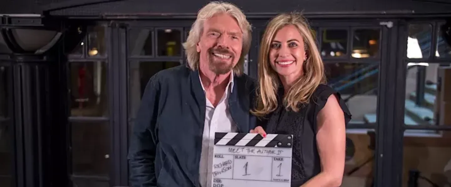 Holly Branson and Richard Branson smiling into the camera holding a movie clipboard