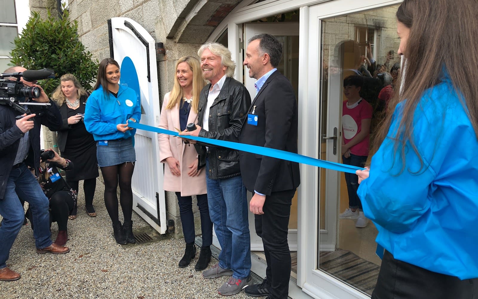 Richard Branson smiling and cutting a blue ribbon to open the new Cool Planet centre