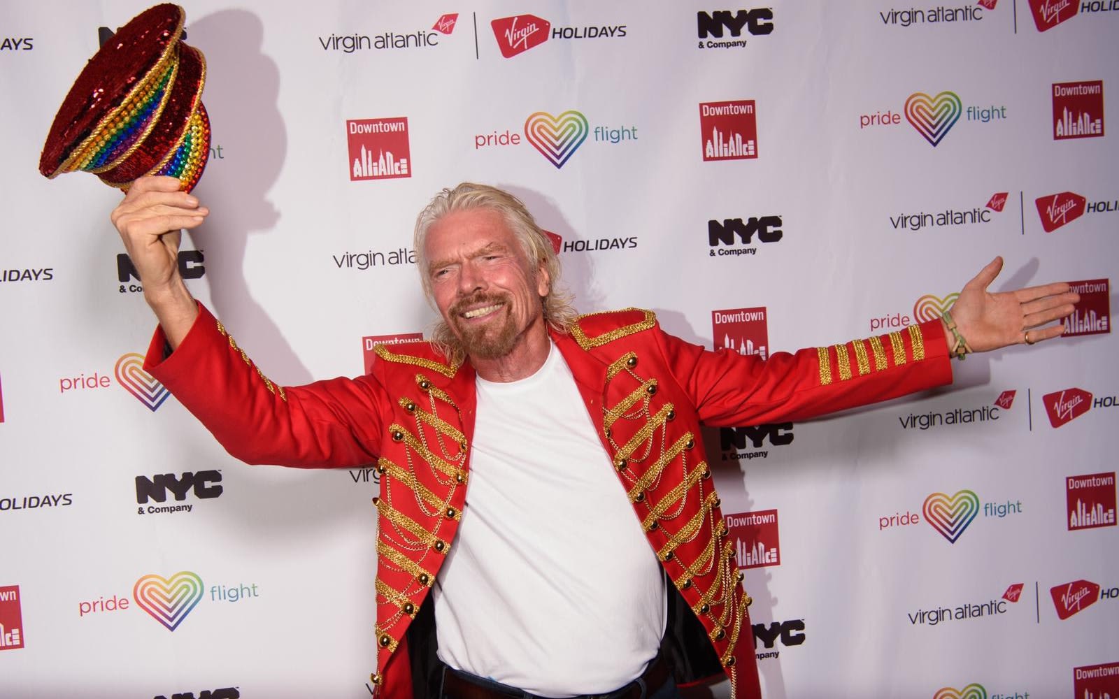 Richard Branson smiling, waving his hat and arms in the air at a Virgin Atlantic Pride event in New York