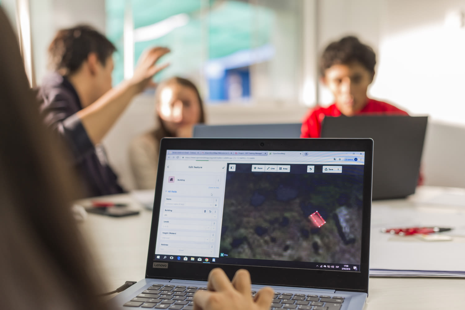 A laptop screen showing the mapping process, with three people out of focus in the background