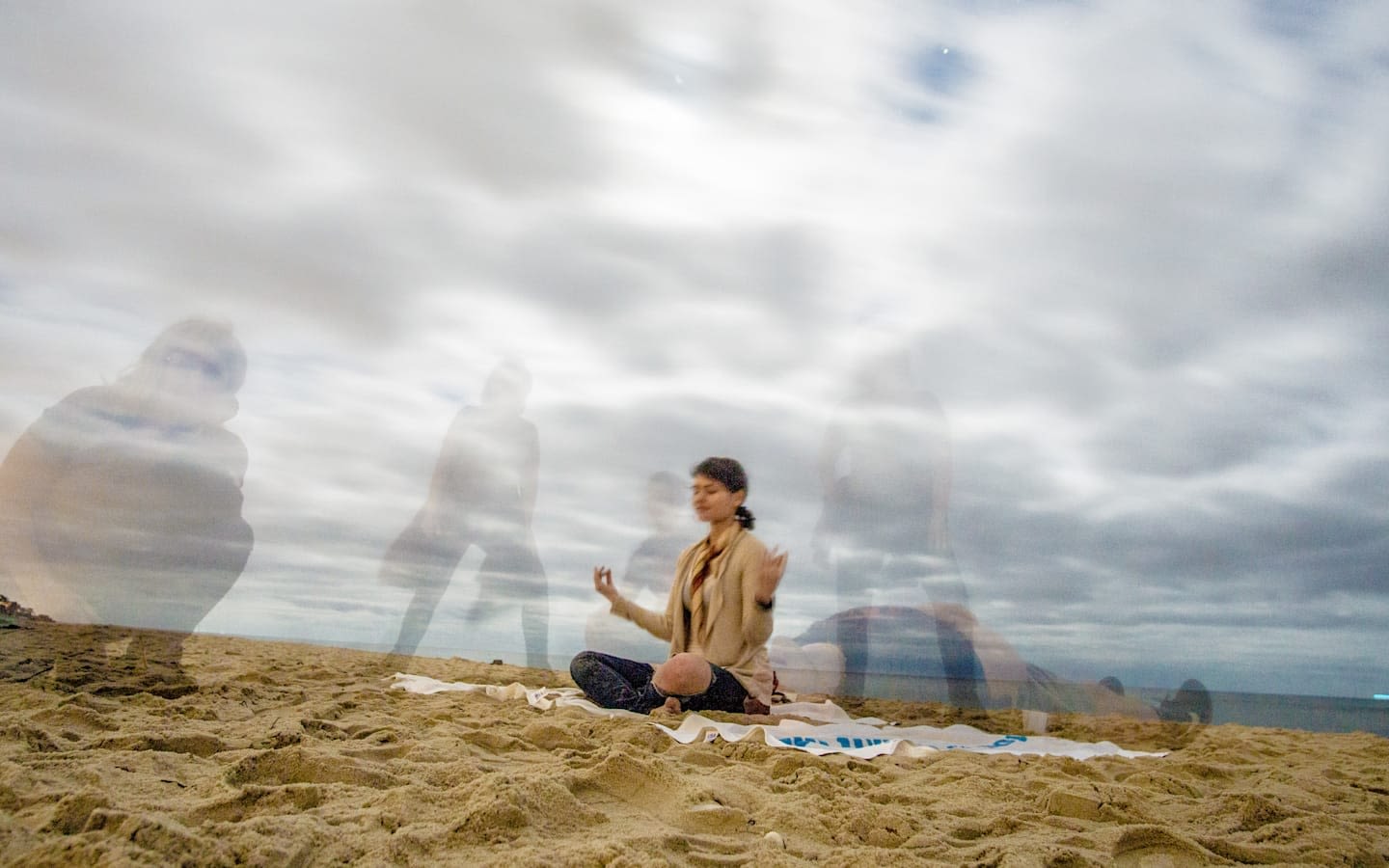 Dr Kate Stone meditating on a beach, with shadows of others around her.